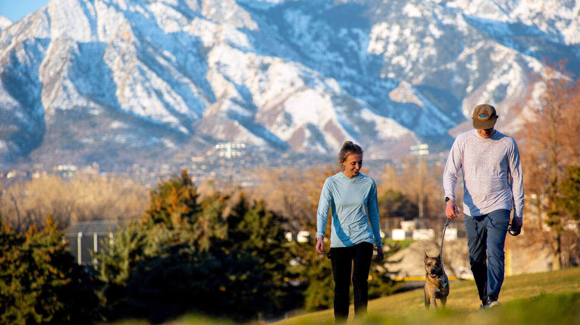 two people walking in a field near mountains